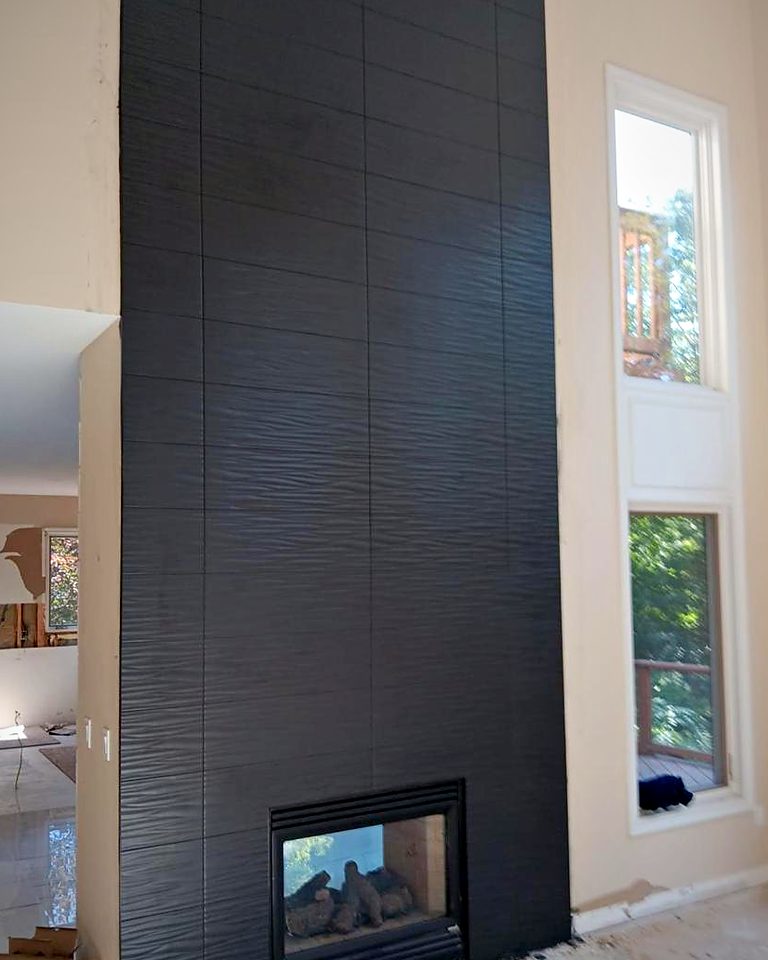 Two-story fireplace chimney clad in black ribbed tile with a see-through gas fireplace