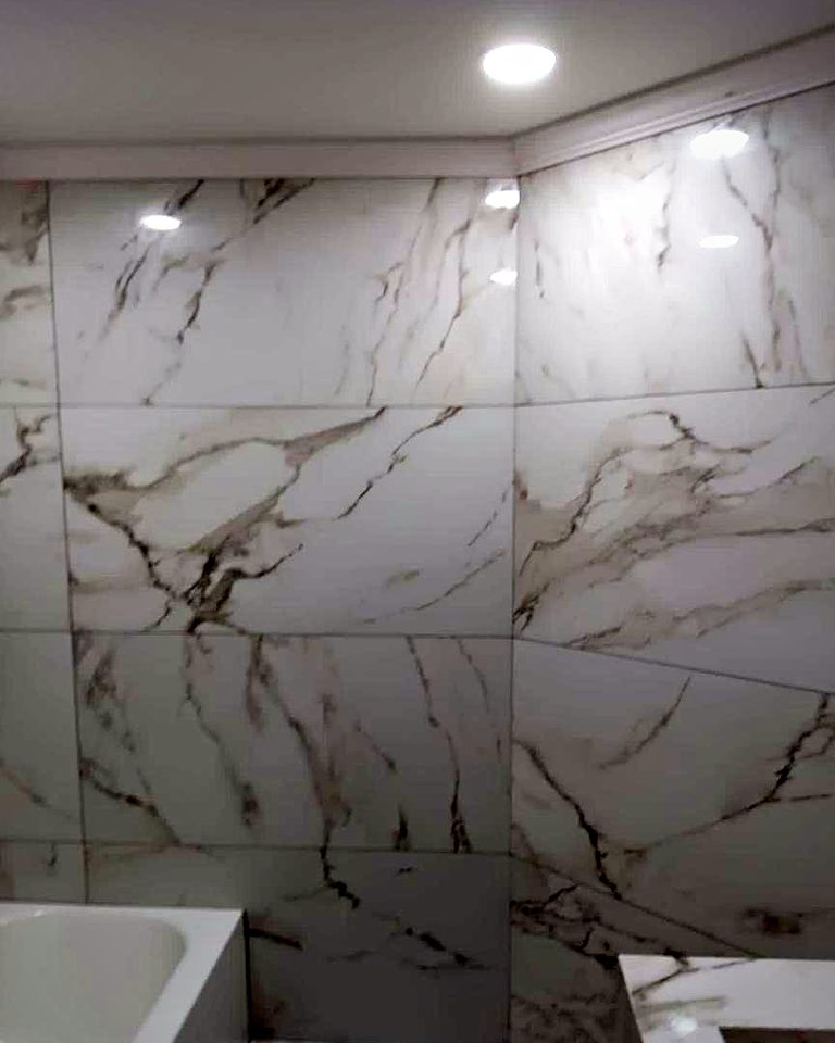 Bathroom with large-format white marble-look tile from floor to ceiling around a tub