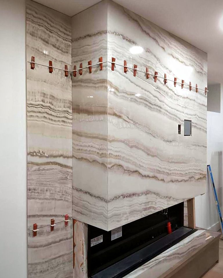 Leveling clips still in place while onyx-look slabs are set around a linear fireplace