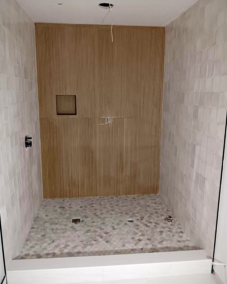 Walk-in shower with a wood-look accent wall, recessed niche and pebble stone floor